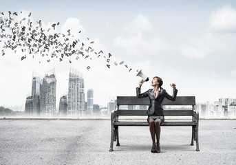 Young woman with megaphone sitting on wooden bench