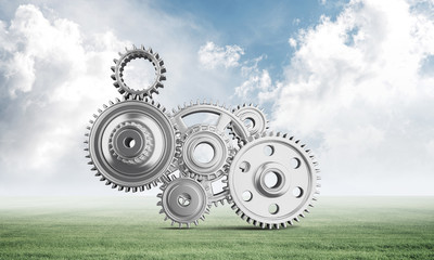 Abstract mechanism with cogwheels on green meadow