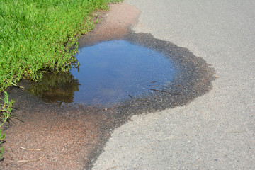Puddle photo. Pot hole or pothole image of a broken cracked asphalt pavement with a dirty water puddle as a transportation symbol of road maintenance and car insurance risk to auto suspensions.