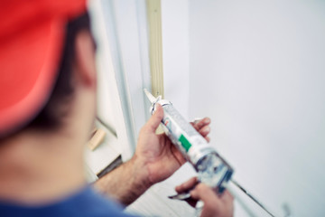 Naklejka premium Worker using silicone for walls and door frame inside the house - renovation fixes.