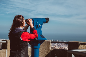 Woman looking at the city of Barcelona from Tibidabo, using a coin operated pair of binoculars.