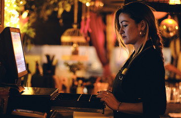 Concepto pequeño negocio o emprendimiento personal: una joven camarera en la máquina registradora de un bar o restaurante