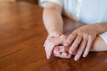 Elderly mother and her daughter holding hands while sitting at the table.Close up on women of different generations holding hands. Close Up Shot Of Mother And Daughter's Hands Holding