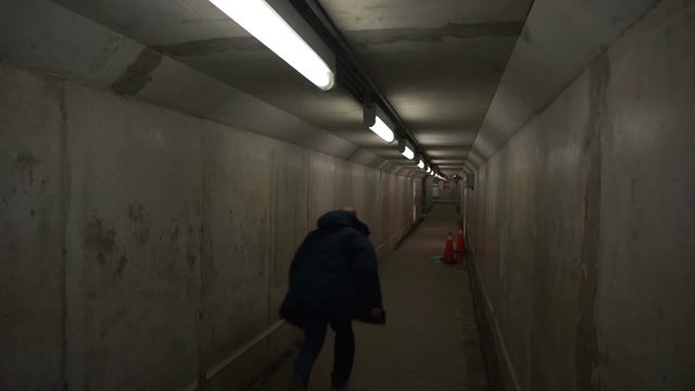 Man running through small concrete subterranean tunnel. One man, alone, walking through an empty concrete subterranean pedestrian tunnel lines with lights and reflective metal. It is under a GO train