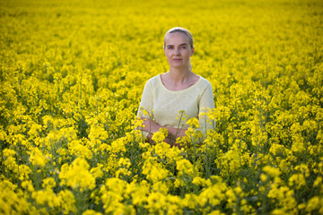 Fototapeta premium Happy woman on blooming rapeseed field in springin yellow blouse.
