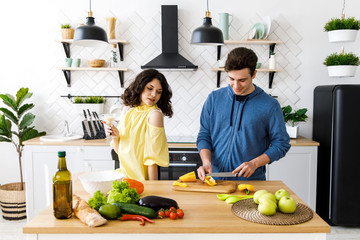 Young cute smiling couple cooking together at kitchen at home. A couple - a girl and a boy who spend time together for cooking