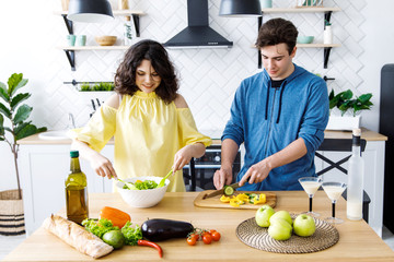 Young cute smiling couple cooking together at kitchen at home. Young people are preparing a salad in a good kitchen