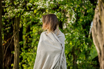 a young girl wrapped in a blanket is standing in a meadow near the trees during sunset