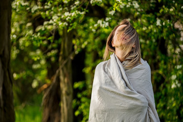 a young girl wrapped in a blanket is standing in a meadow near the trees during sunset
