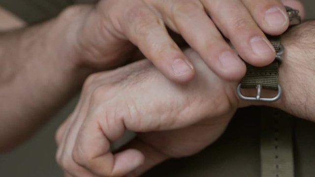 Closeup of the hands of men in khaki clothes, worn on the wrist of the diver's watch on nylon strap.