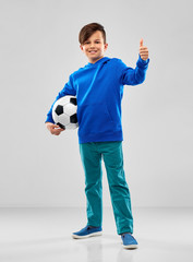 childhood, football and sport concept - smiling boy in blue hoodie with soccer ball showing thumbs...