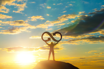 A silhouette of a man holds an infinity symbol on top of a mountain with a sunset background. Concept idea, life, success, business.