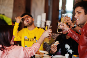 Group of asian friends eating pizza and cheering during party at pizzeria. Happy indian people having fun together, eating italian food and sitting on couch.