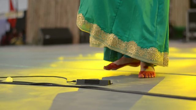Shot of dancing feet of female Indian classical Kathak dancer decorated with red alta & ghungroo, wearing green skirt with golden border performing on the beats of the tabla (percussion instrument).