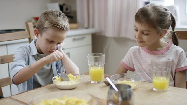 boy dont want to eat his cornflakes but mother makes him, and he laughed by his sister