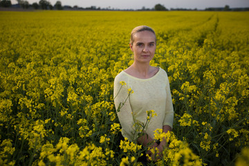 Fototapeta premium Happy woman on blooming rapeseed field in springin yellow blouse.