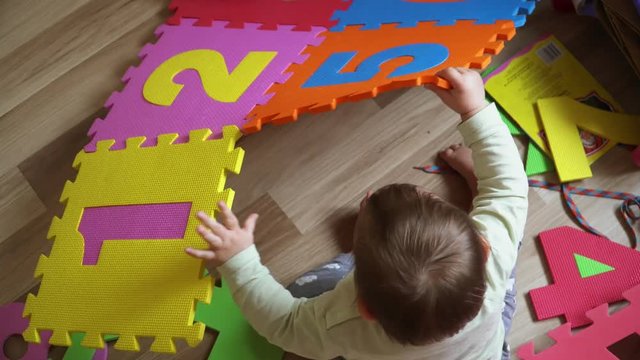 Toddler girl on ht efloor at home playing with foam mat puzzle with numbers, early development