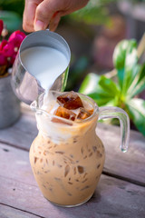 Pouring milk in a glass with latte coffee and iced