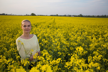 Fototapeta premium Happy woman on blooming rapeseed field in springin yellow blouse.