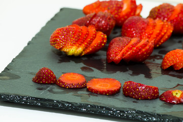 Sliced ​​strawberries on a natural stone serving platter and two strawberries in the whole oyster-shaped plate