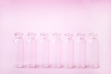 Group Medicine vials with open neck without stopper. Empty glass medical ampoules in a row on a light pink background. Vaccines, Medicine, Immunization concept.