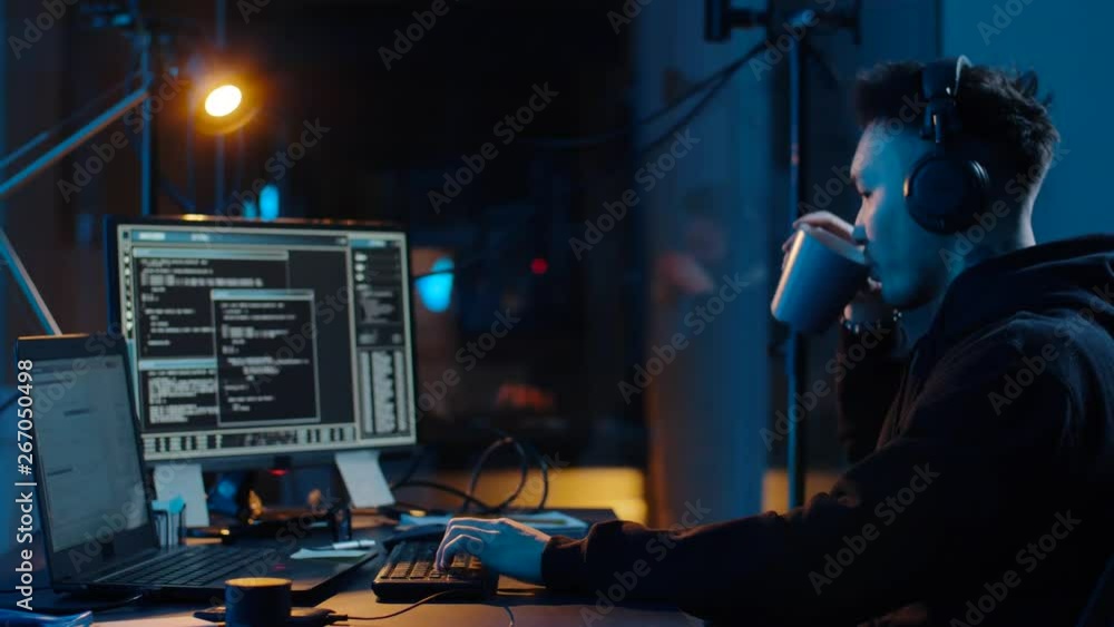 Poster cybercrime, hacking and technology concept - asian male hacker in headphones with coding on laptop c