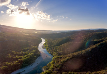 Fototapeta na wymiar Stunning aerial drone shot of the Rhone river at sunrise. The river reflects the early morning sun and the river gorge is forested and green. An old roman bridge can be see in the distance.
