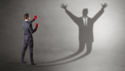 Businessman with boxing gloves fighting with disarmed businessman shadow
