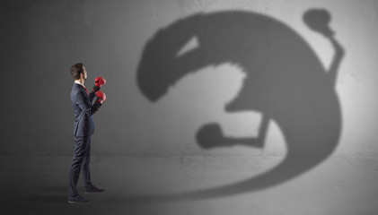 Businessman with boxing glove fighting with a big monster shadow
