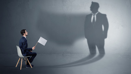 Humble businessman staying and offering stuffs to a huge angry bull shadow
