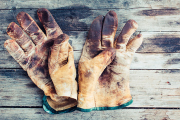 Worn leather work gloves on wood background, stained with grease and industrial oil
