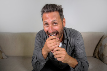 young attractive and happy man laughing at home watching television show or comedy series holding...