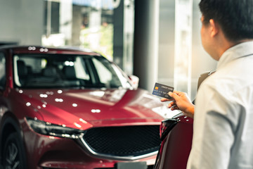 Fototapeta premium Asian man holding credit card for car blurred bokeh background e-shopping