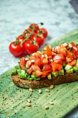 On a green plate of brusket with tomatoes and avocado. Light gray textured background. Beautiful serving of dishes. Restaurant menu