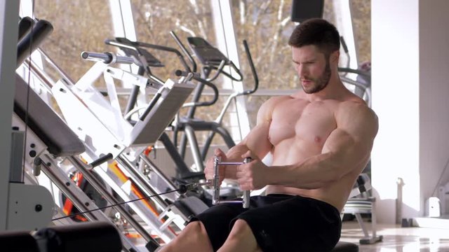 power training, nude bodybuilder male with bare-chested doing muscle building workout on traction simulator while working on body at gym