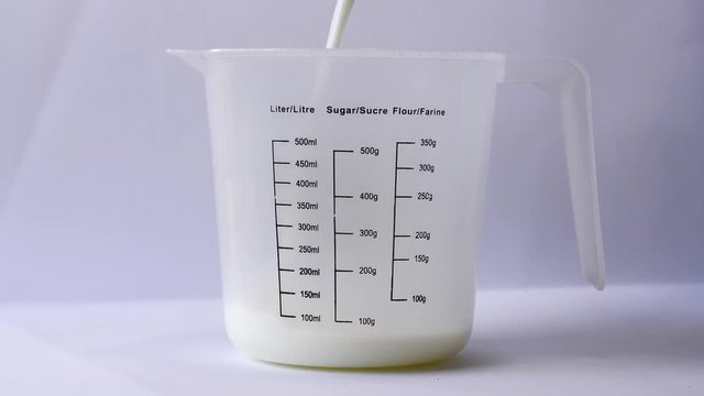 300 ml of milk pouring into Plastic Graduated Measuring Beaker Liquid Cup Container. slow motion pouring milk.