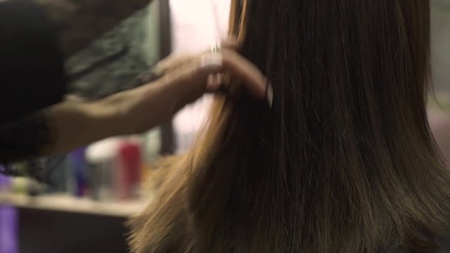 hairstylist with trendy ring on left hand trims beautiful dark hair ends with silver scissors and comb close view