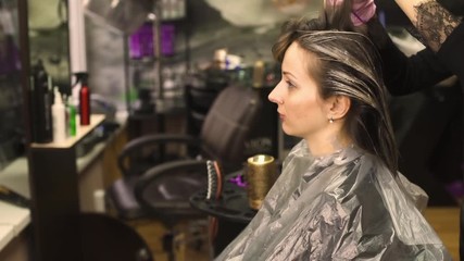 skilled stylist in black lacy shirt and bright pink latex gloves dyes slim young lady brown hair close view