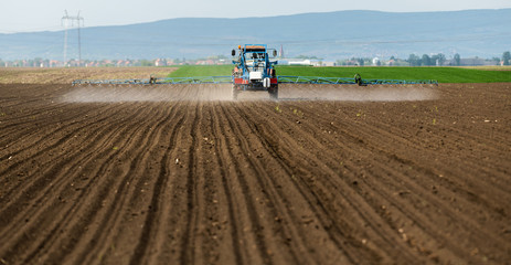 Fototapeta premium Tractor spraying pesticides at wheat field
