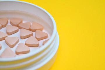 Pink triangular unusual pills in a white round box on a yellow background with copyspace, side view, macro