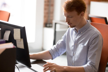 Focused redhead male employee working on pc in office