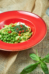 Spaghetti with fresh green peas. Gray textured background with beige fabric. Beautiful serving of dishes. Restaurant menu