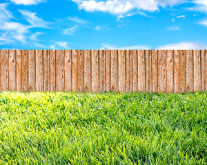 Wooden garden fence at backyard, green grass and blue sky with white clouds