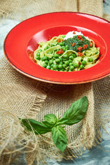 Spaghetti with fresh green peas. Gray textured background with beige fabric. Beautiful serving of dishes. Restaurant menu