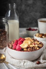 healthy breakfast granola in a plate with nuts, banana and raspberries, copy space