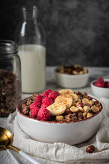healthy breakfast granola in a plate with nuts, banana and raspberries, copy space