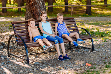 Two boys and a girl sitting on a bench in the summer. Three children