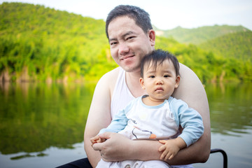 Portrait of baby girl and her daddy sitting on floating house with beautiful river and mountain landscape in background