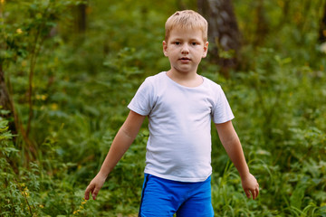 serious seven year old blond boy in white t-shirt natural background in summer.