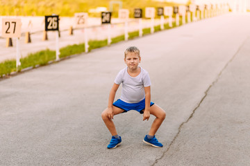 funny seven-year-old boy in blue shorts and sneakers is on the pavement in the summer.